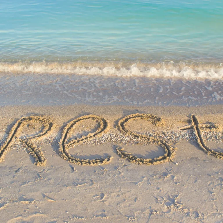 The word "REST" written in the sand on a peaceful beach, symbolizing the restorative sleep that can be achieved by balancing the body's biofield and energy.