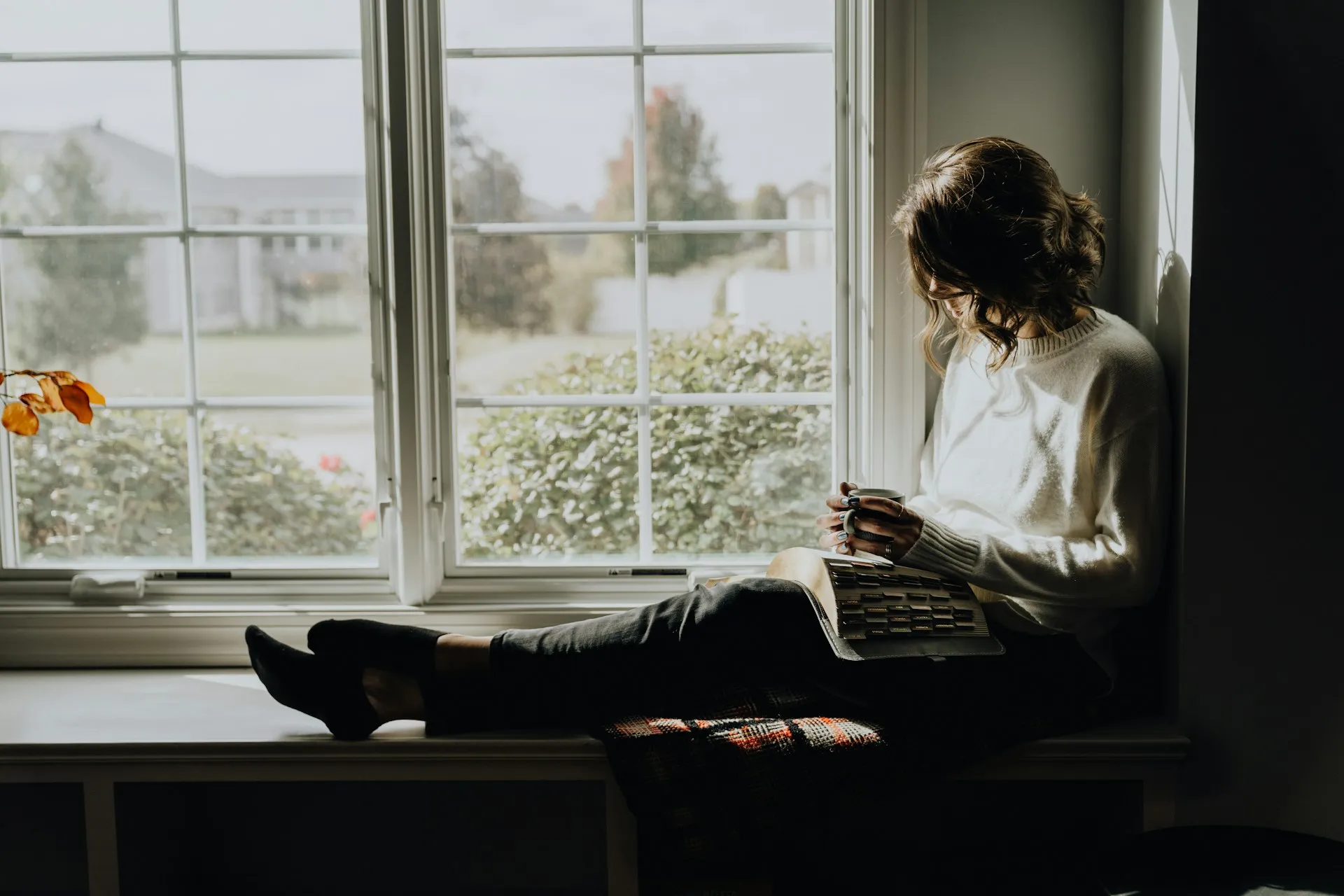 A woman sitting peacefully by a bright window holding a warm mug, reflecting on her body's available capacity for healing under chronic stress.