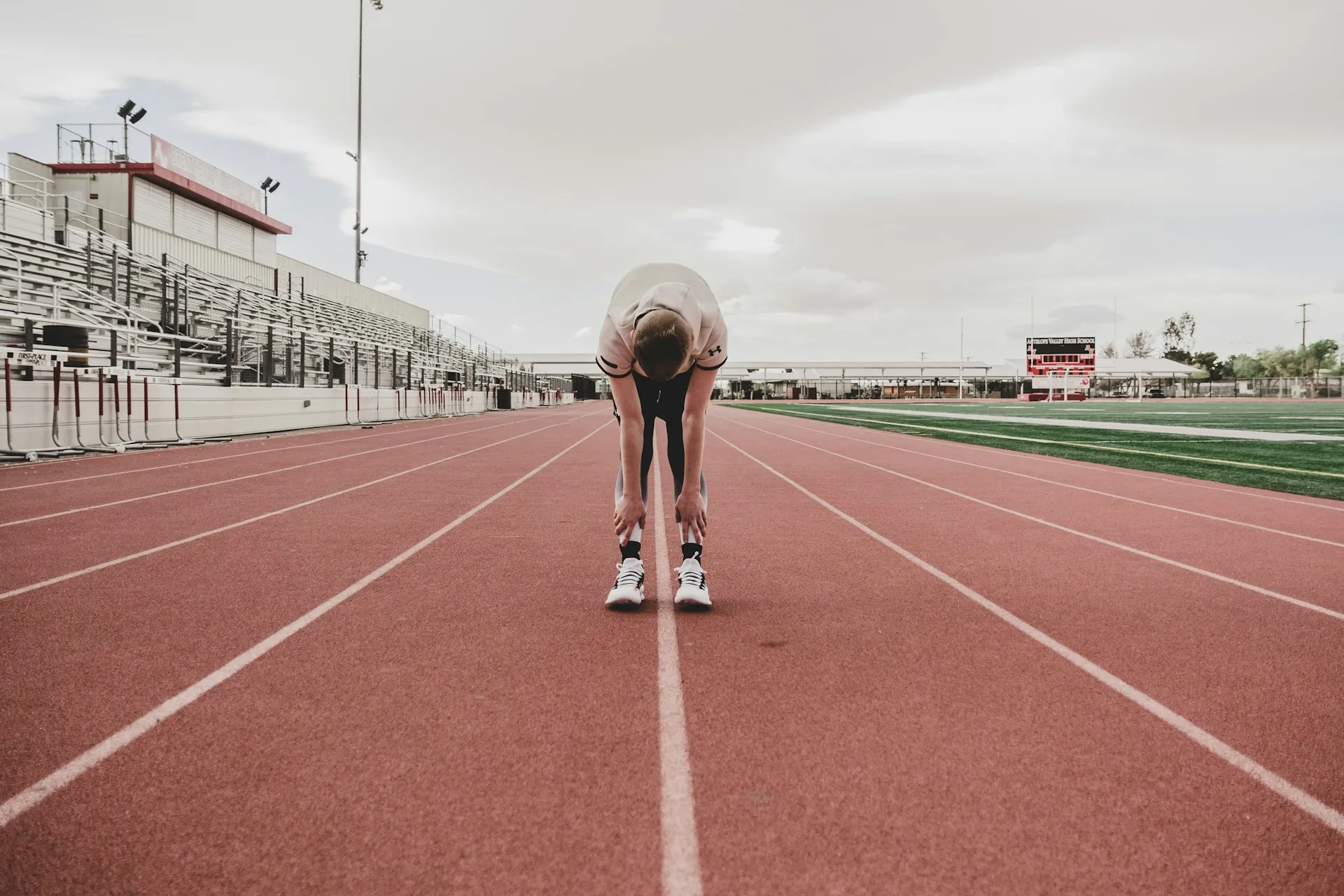 Athlete bending forward to stretch alone on an empty red running track