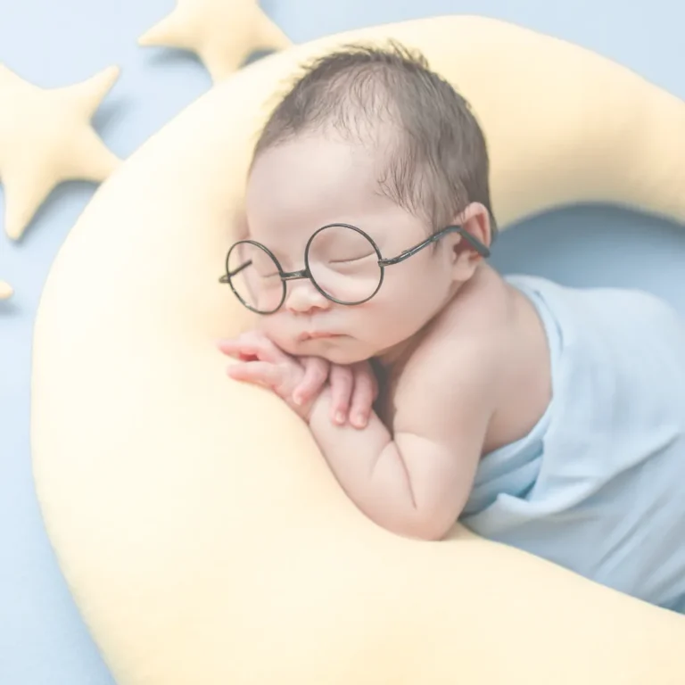 Newborn baby wearing glasses, peacefully sleeping on a moon-shaped cushion with stars in the background