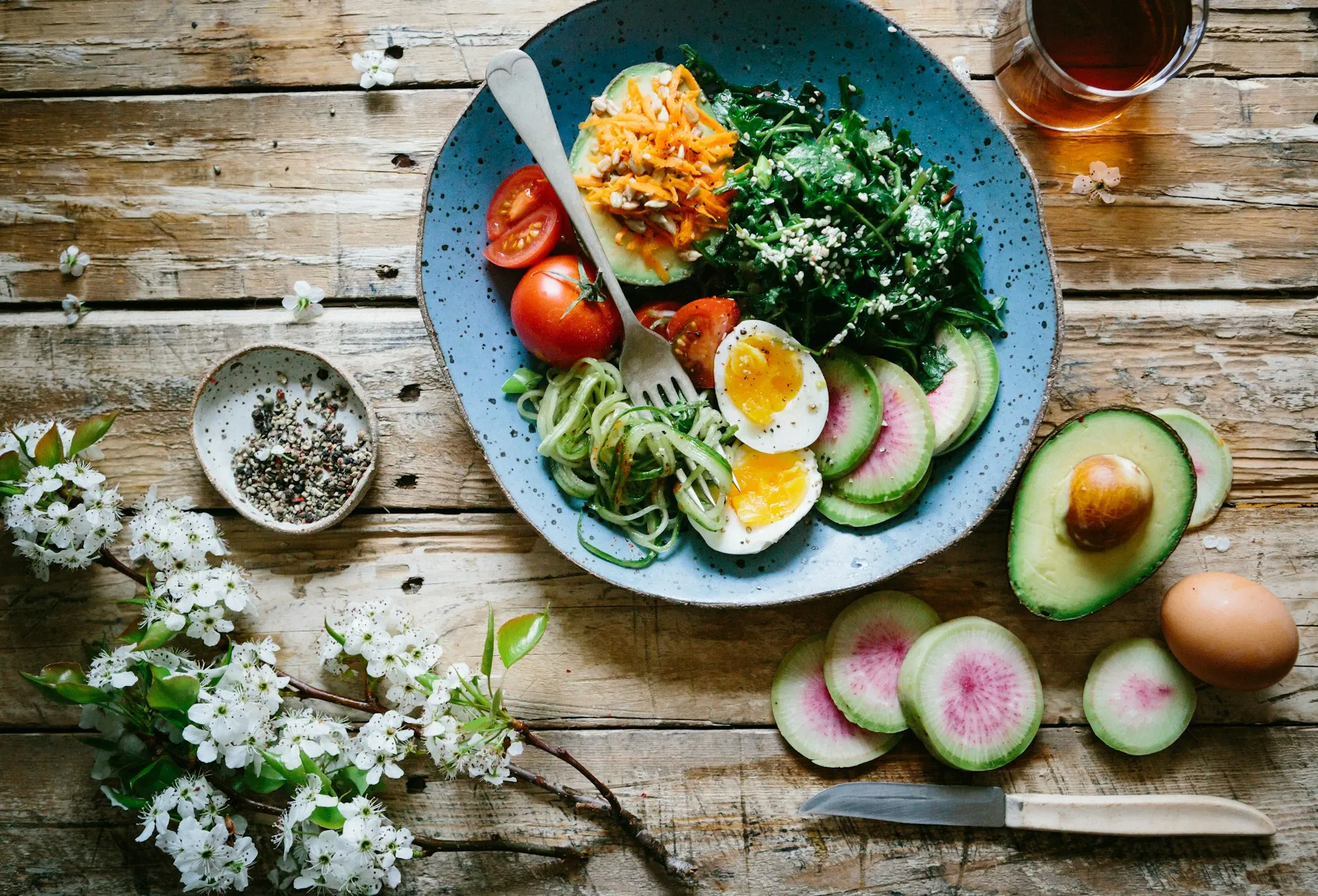 Overhead view of a blue plate with soft-boiled egg, avocado, tomatoes, greens, and radish on a rustic table