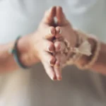 A close-up of a person's hands in a mindful meditation pose with mala beads, representing the energetic realignment and biofield balancing of a med-cation.