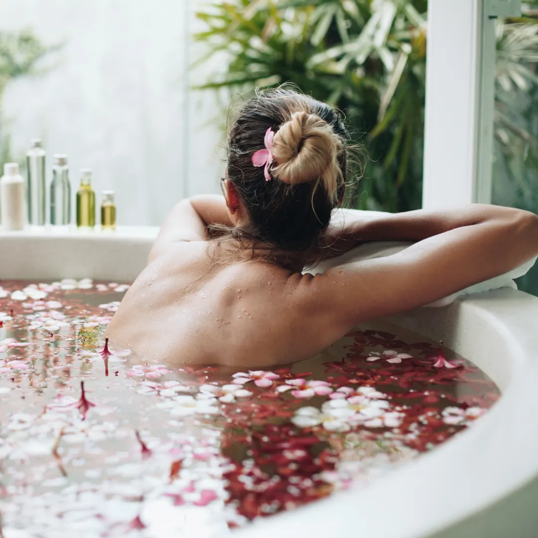 A woman relaxing in a bath with flower petals, integrating aromatherapy and biofield healing.