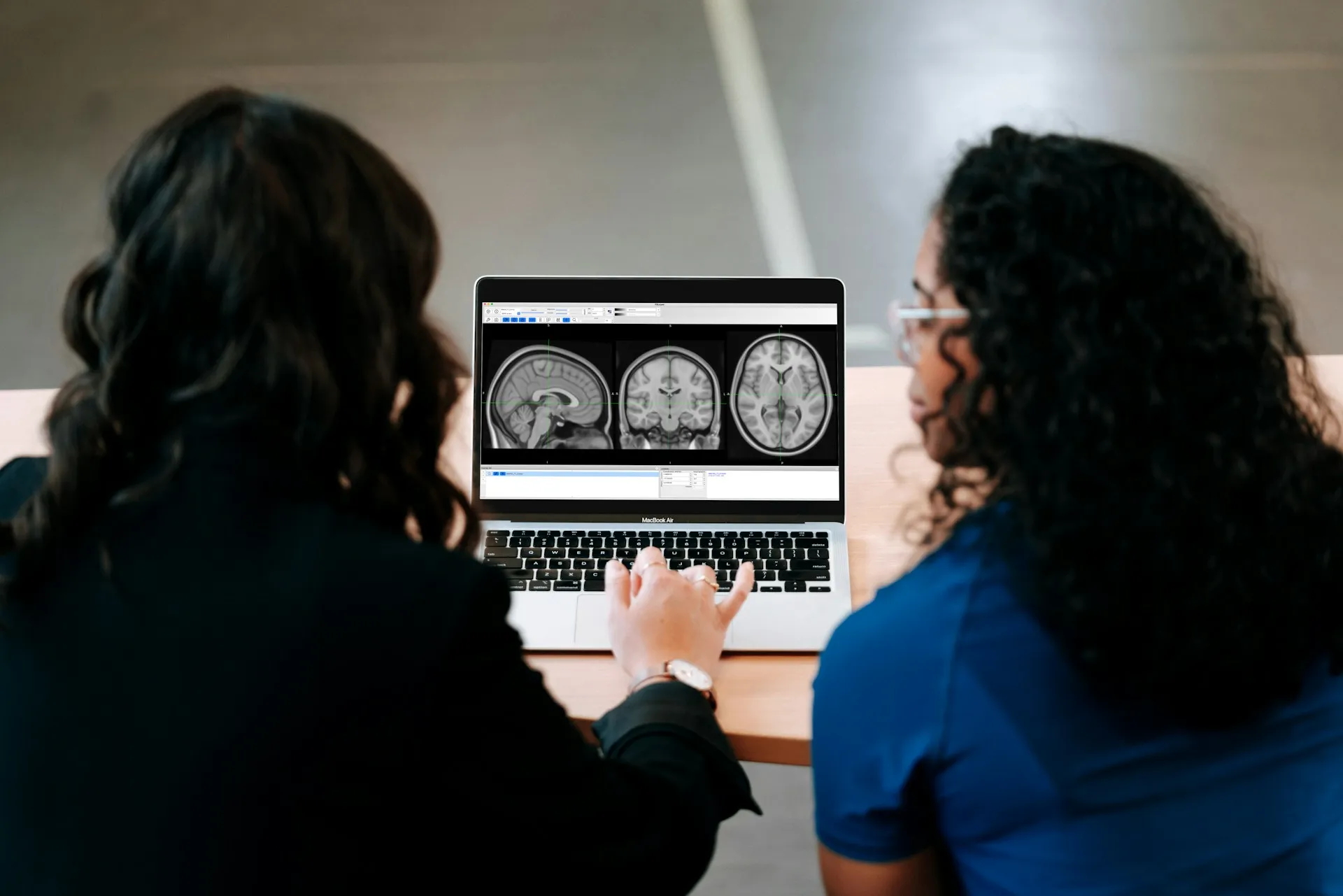 Two researchers reviewing sagittal, coronal, and axial brain MRI scans on a laptop