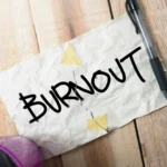 A torn piece of paper with the word "BURNOUT" written in black marker, symbolizing the breaking point of chronic stress.