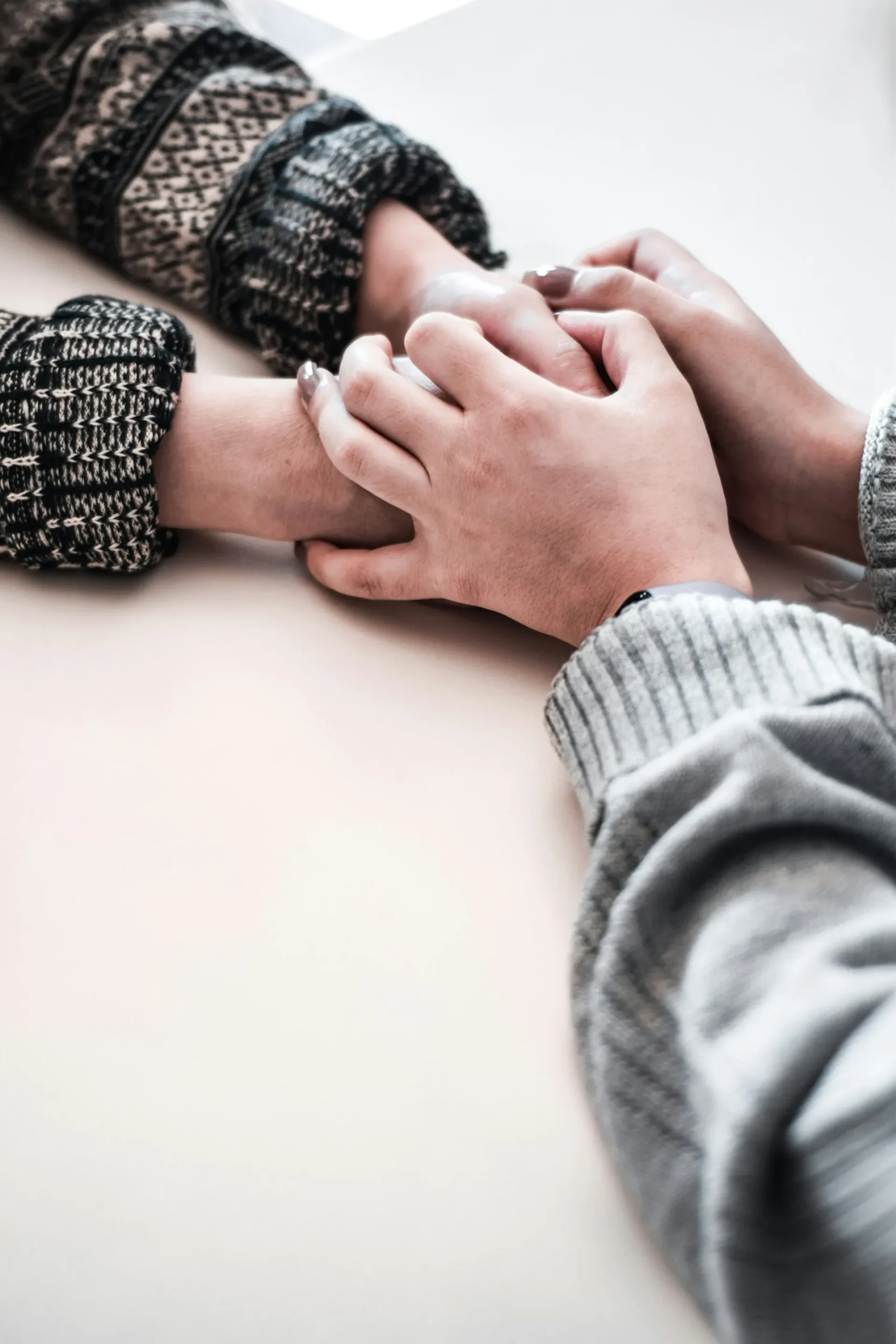 Two people's hands clasped together on a pale table, both wearing knit sweaters