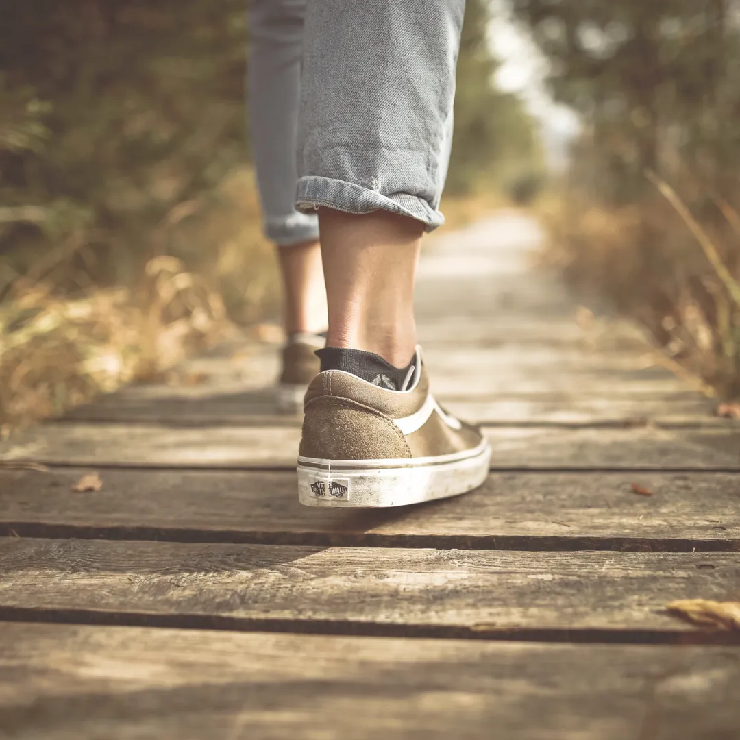 A close-up of a person's feet in sneakers taking a mindful step on a wooden boardwalk, illustrating the core practice of silent walking.