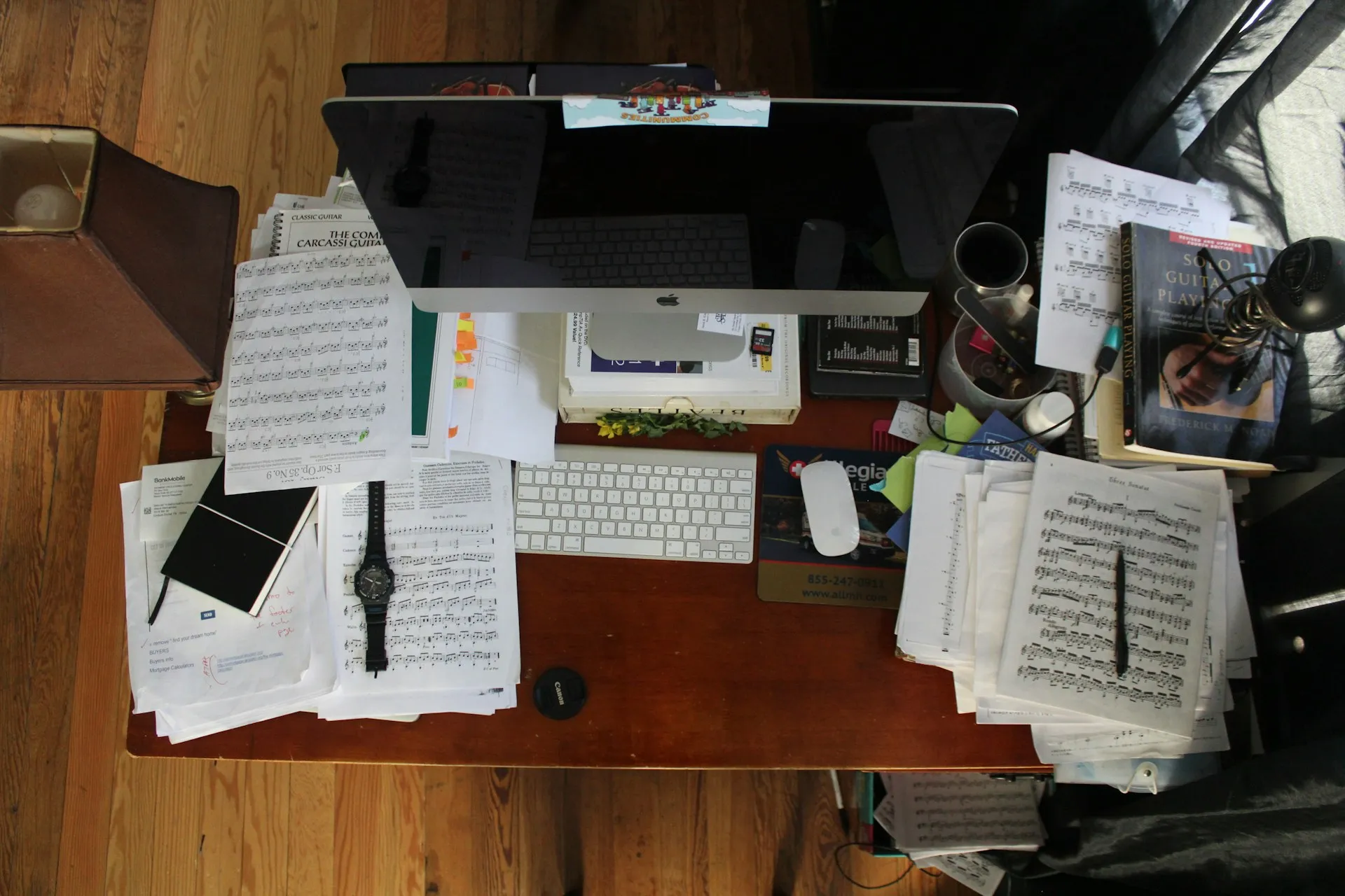 Overhead view of a cluttered desk covered in sheet music, papers, books, and a computer