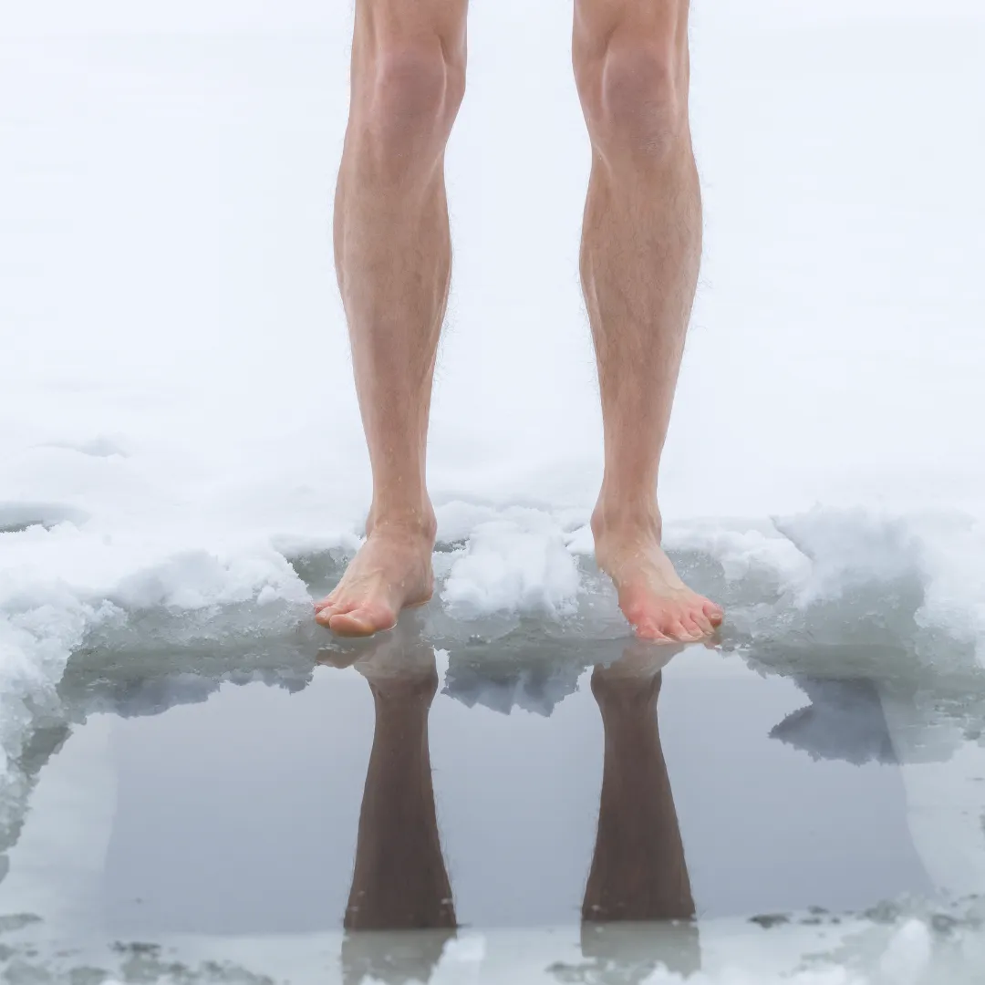 Athlete's bare legs standing in an ice hole during a cold plunge therapy session for muscle recovery.