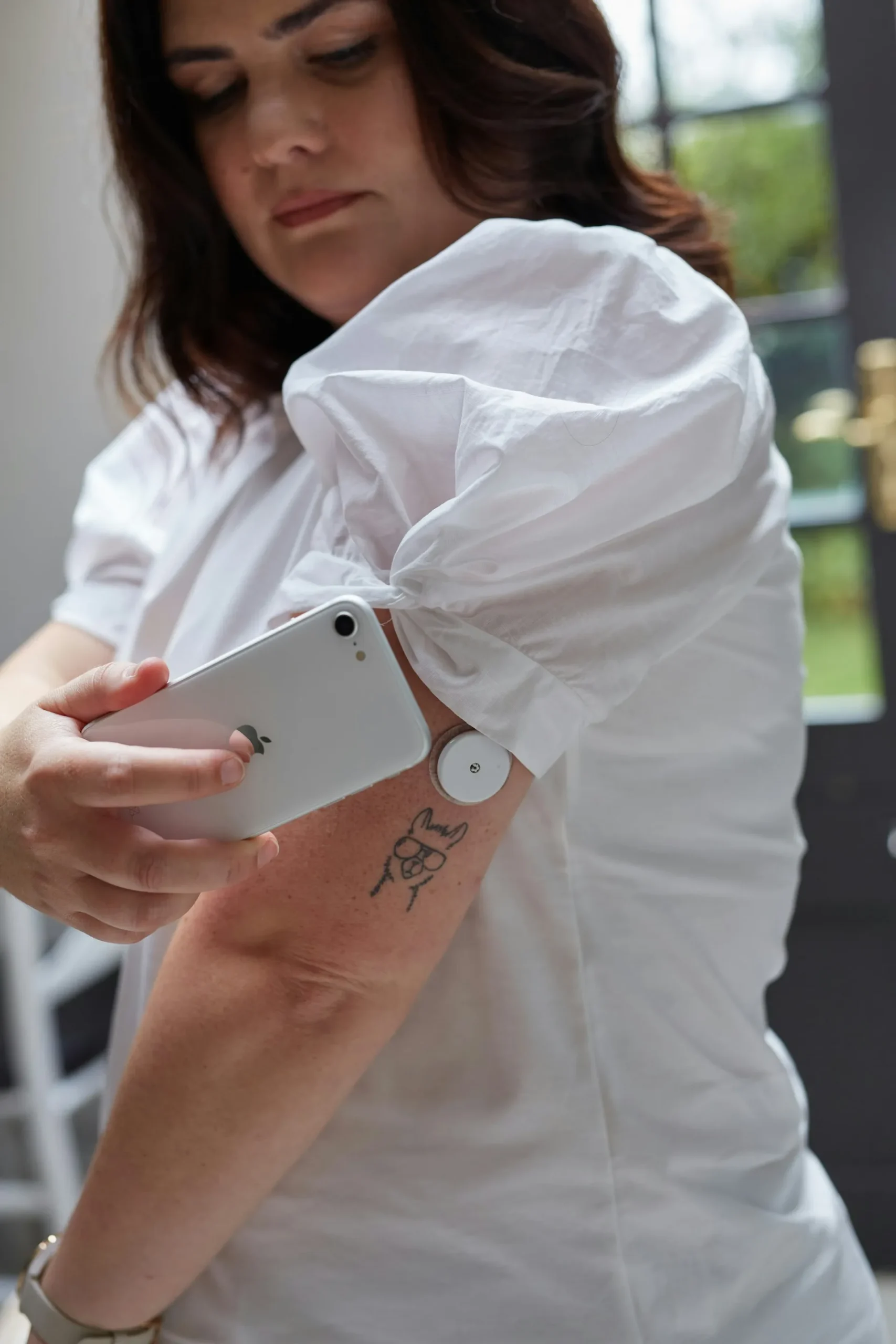 Woman scanning a continuous glucose monitor sensor on her upper arm using a smartphone