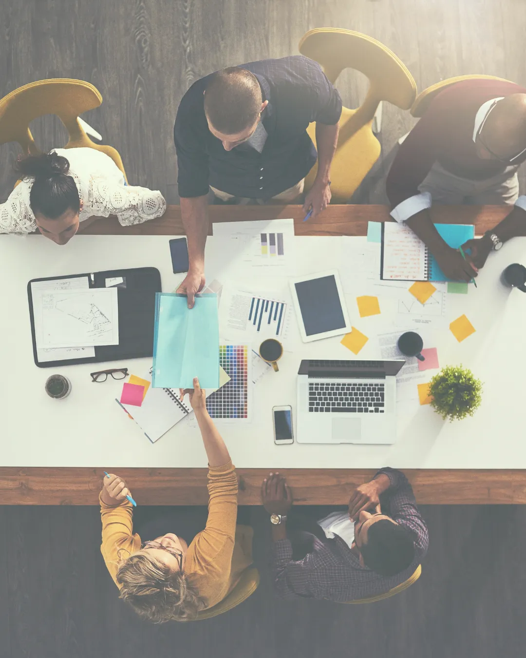 An overhead view of a diverse team working together at a table, with documents, laptops, and strategy discussions on preventing burnout in the workplace.