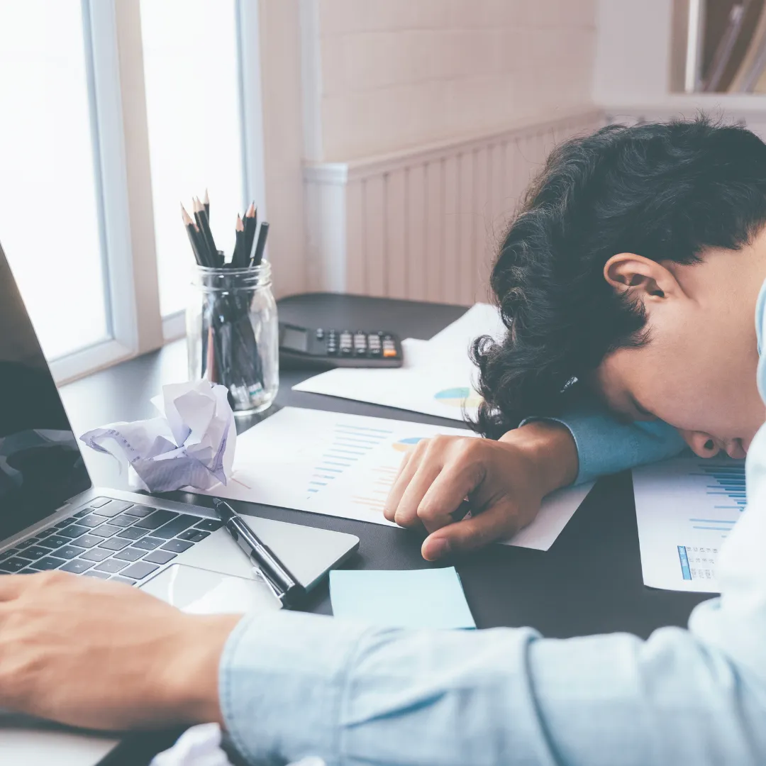 An overhead view of a person with their head in a notebook on a desk, surrounded by crumpled paper, symbolizing the burnout and mental exhaustion caused by decision fatigue.