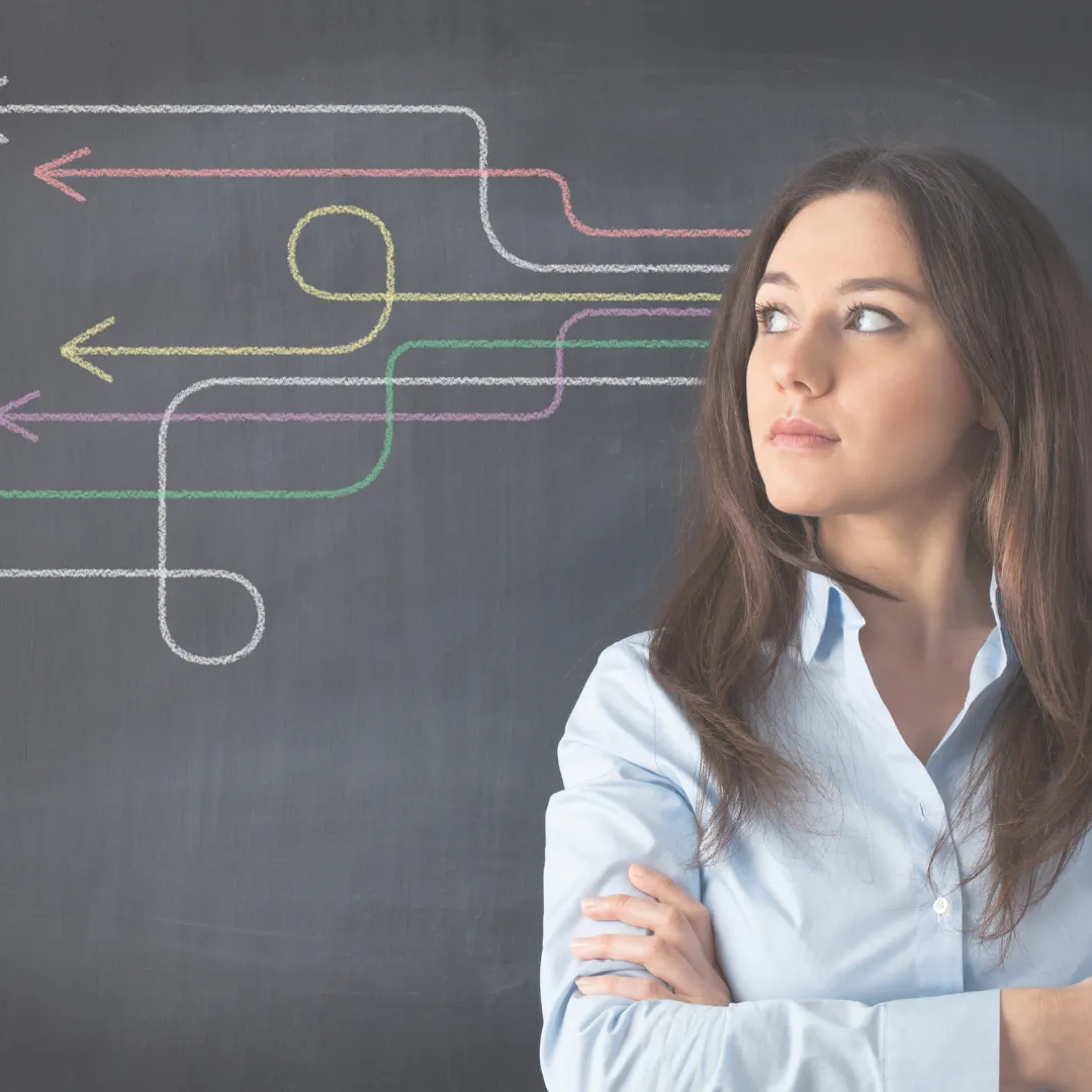A woman with arms crossed contemplates a series of tangled, colorful arrows on a chalkboard, illustrating the mental state of cognitive overload from decision fatigue.