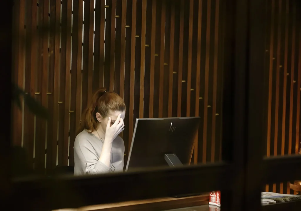 Exhausted woman holding forehead in front of a computer screen showcasing digital overload and autonomic nervous system stress.