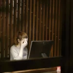 Exhausted woman holding forehead in front of a computer screen showcasing digital overload and autonomic nervous system stress.