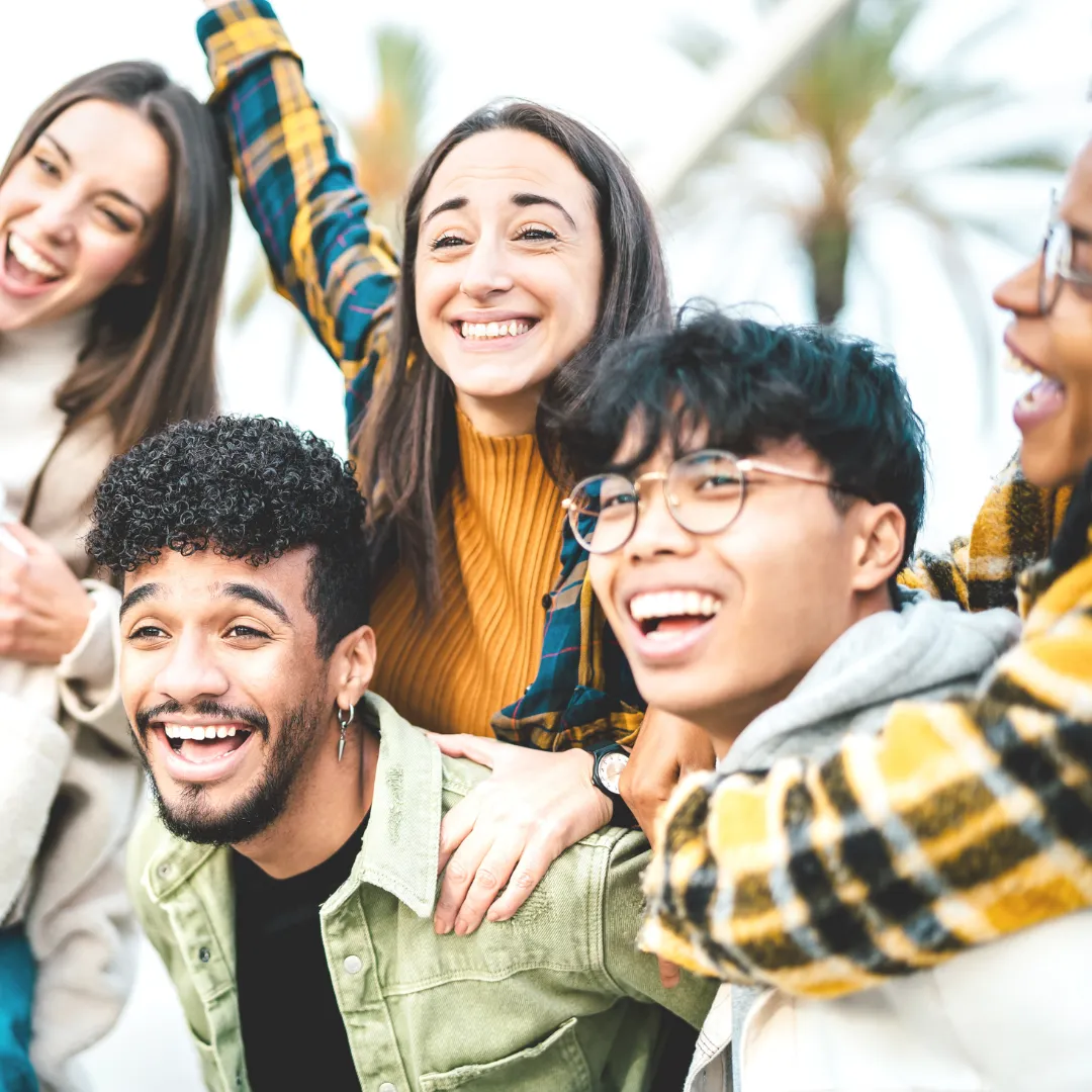 A diverse group of happy Gen Z adults laughing together outdoors, illustrating the broad cultural shift of Gen Z using ChatGPT for personal support.