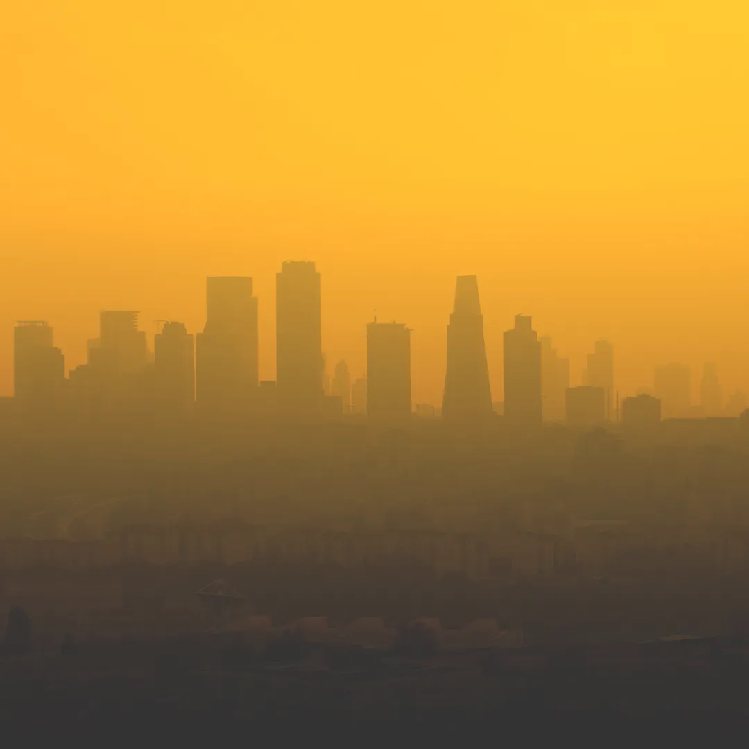 A city skyline shrouded in a thick orange haze, visualizing the concept of E-smog or electromagnetic pollution in a modern urban environment.