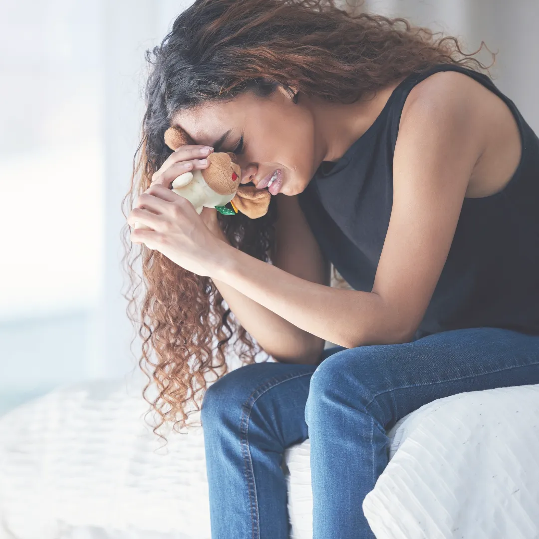 Young woman crying and holding a teddy bear, showing emotional distress and unresolved trauma.