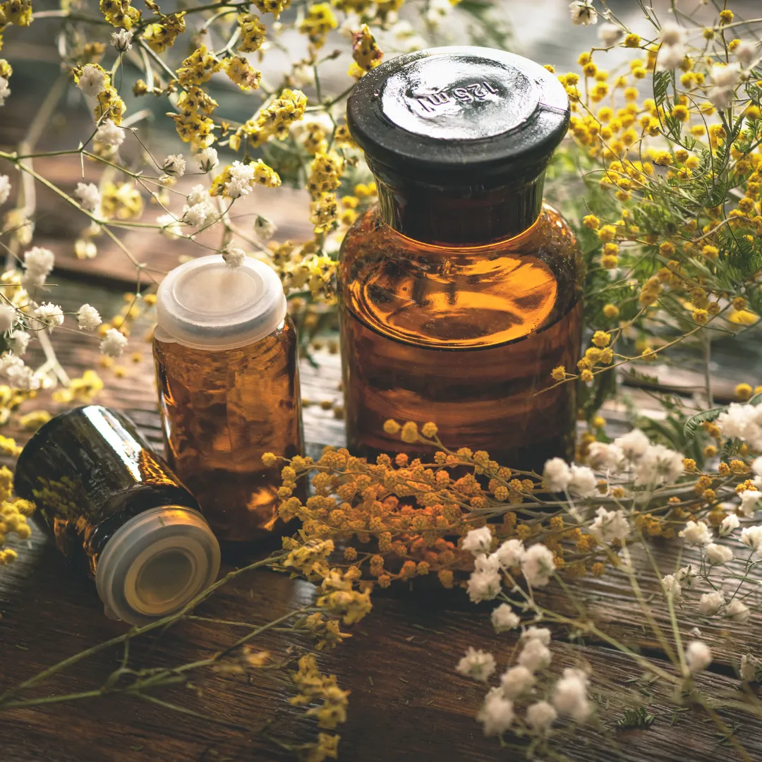 Brown apothecary bottles and tinctures on a wooden table, surrounded by dried yellow flowers, representing personalized supplement regimens in functional medicine.