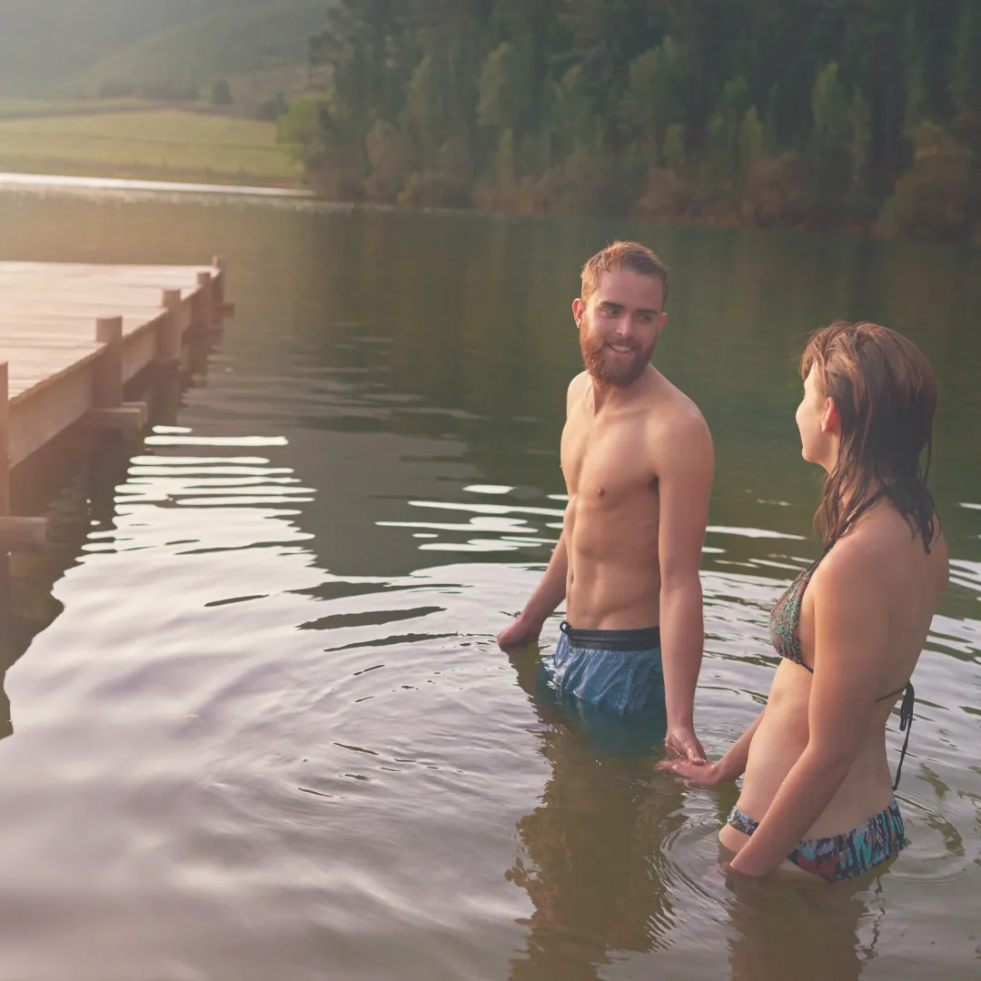 Two people standing in a calm lake near a wooden dock, finding a moment of connection and cool relief during the heat of late summer.