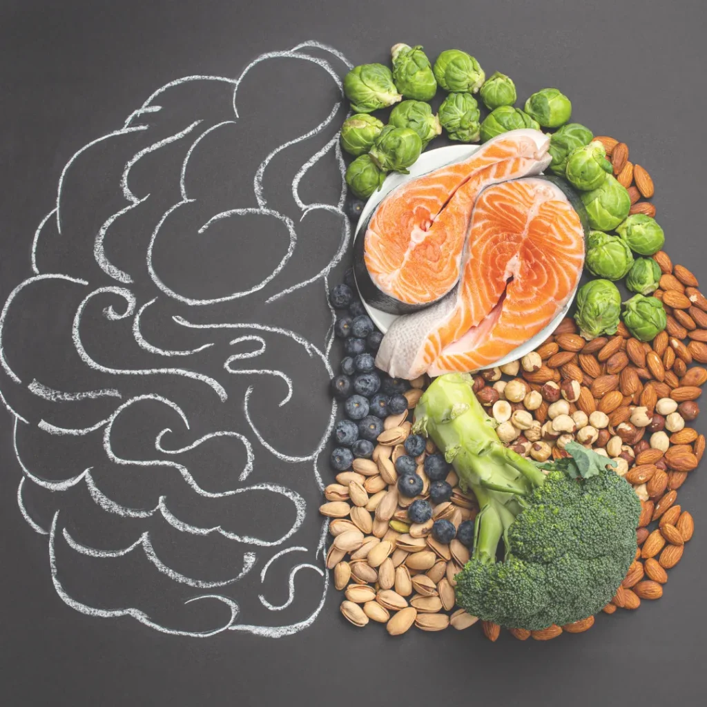 A brain outline on a chalkboard, with one half filled with healthy foods like salmon, nuts, and broccoli, visually representing the gut-brain connection and its role in emotional health.