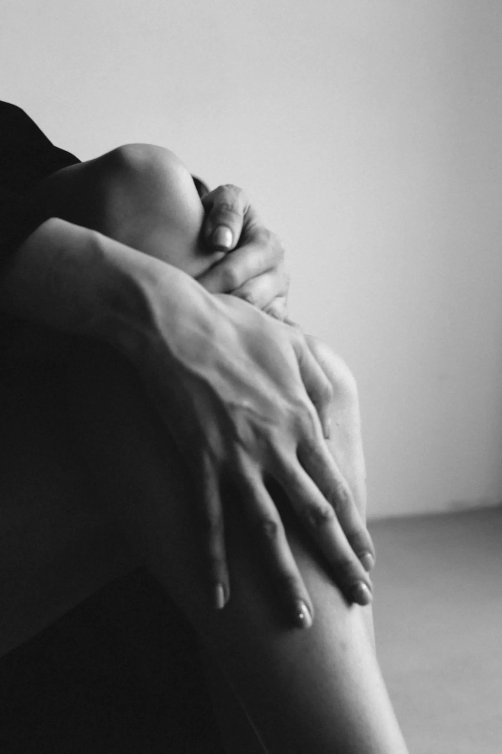 Black and white close-up of two hands clasped around a bent knee