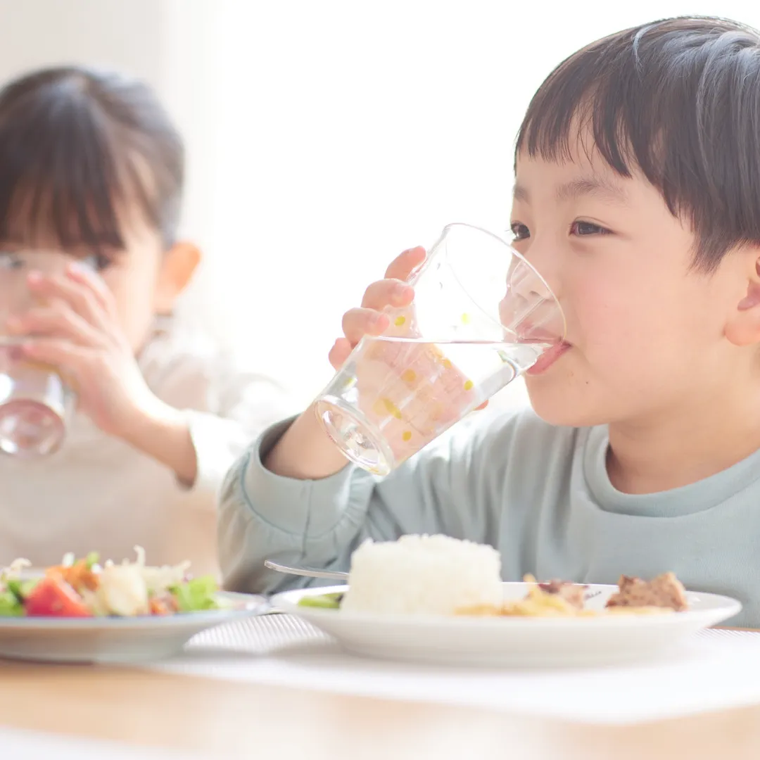 Two young children sitting at a table eating a healthy meal with rice and salad and drinking water, illustrating the importance of foundational dietary patterns.