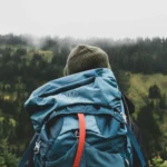 Person seen from behind wearing a rain-flecked backpack looking out over a misty forested hillside