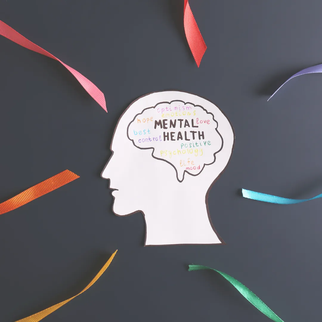 A paper cutout of a human head silhouette with the words 'Mental Health', 'hope', 'love', and 'optimism' written inside, surrounded by colorful ribbons.