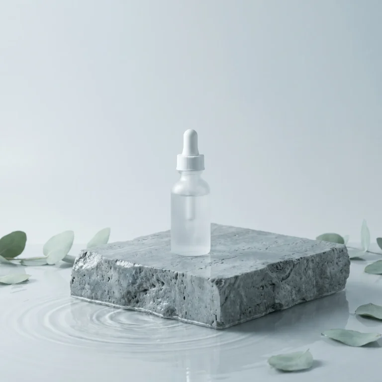 A clear serum dropper bottle on a wet grey stone block surrounded by green eucalyptus leaves in water, symbolizing holistic support for summer fatigue and allergies.