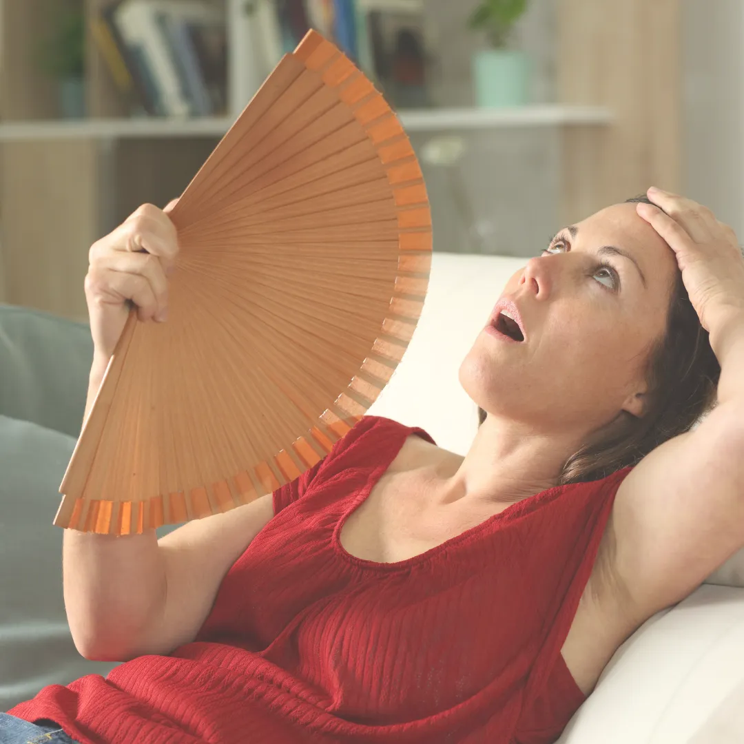 Woman fanning herself due to hot flash, a common symptom during menopause.