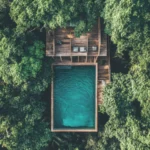 Aerial view of a luxury wellness retreat villa featuring a private pool surrounded by dense green forest, representing a sanctuary for longevity and biohacking.