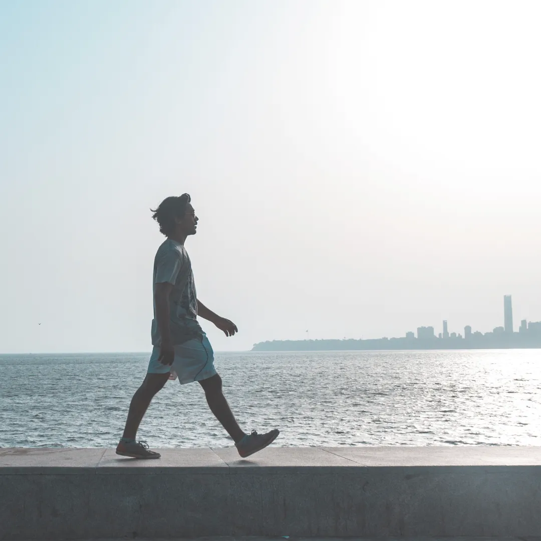 Young man practicing silent walking on a city promenade next to the sea, with a skyline in the background.