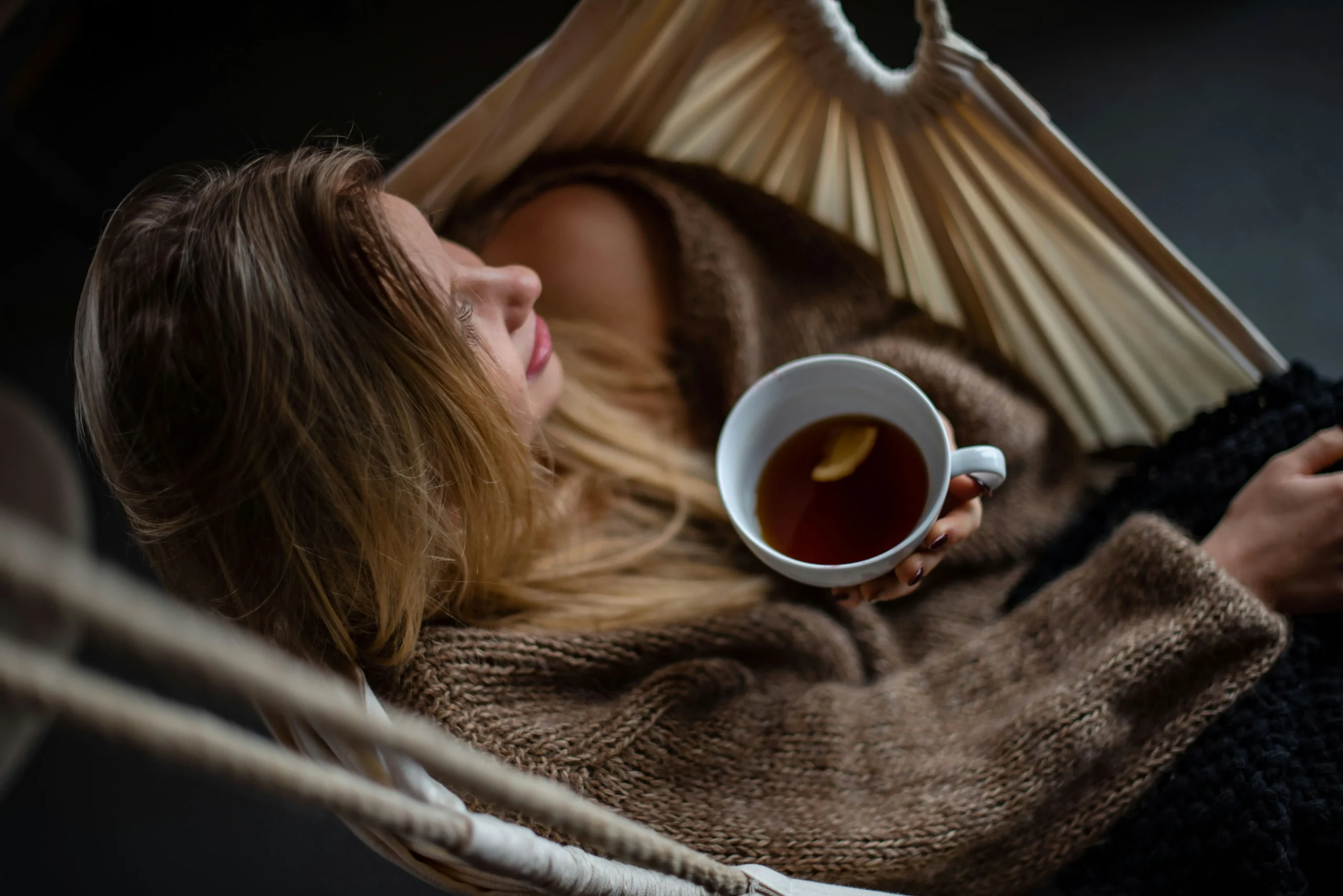 A woman relaxing in a hammock with a warm cup of tea to calm the nervous system and manage stress and digestive issues.