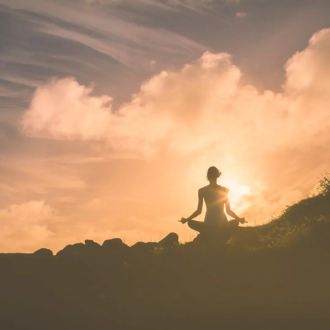 Person meditating at sunrise, practicing grounding for energy healing and stress relief