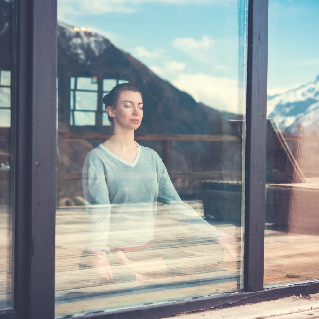 Woman meditating in a quiet Longevity Room with mountain views for mental clarity and energy alignment.