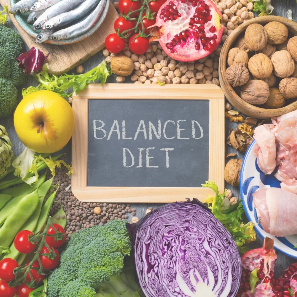 An overhead view of healthy Mediterranean diet foods like fish, walnuts, broccoli, and pomegranate with a small chalkboard that says "Balanced Diet".