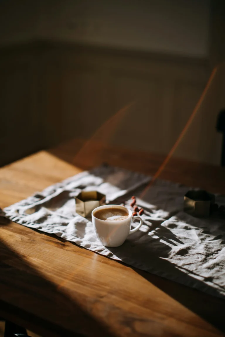 Cup of coffee on a linen runner across a wooden table in soft morning light