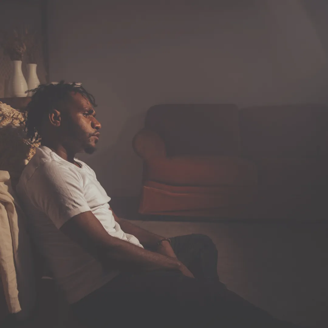 A person sitting alone in a dimly lit room, looking thoughtful and sad, representing the human need for accessible mental health support.