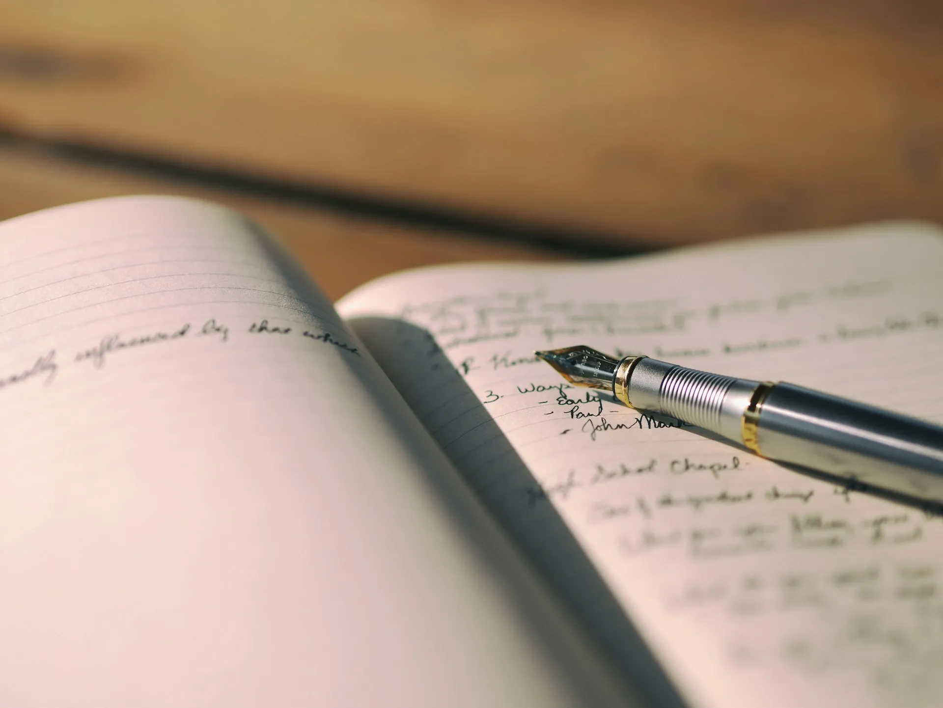 Fountain pen resting on an open notebook filled with handwritten notes on a wooden desk