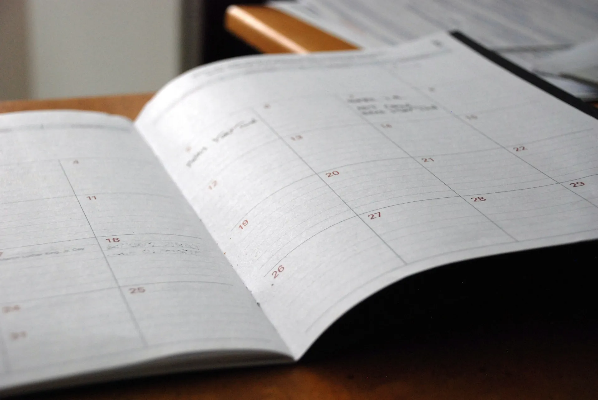 Open paper monthly calendar on a wooden desk with handwritten notes