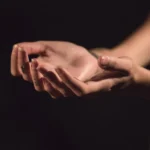 Two open hands held palms-up in soft low light against a dark background