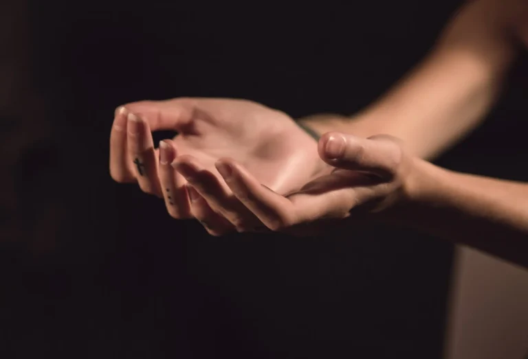 Two open hands held palms-up in soft low light against a dark background