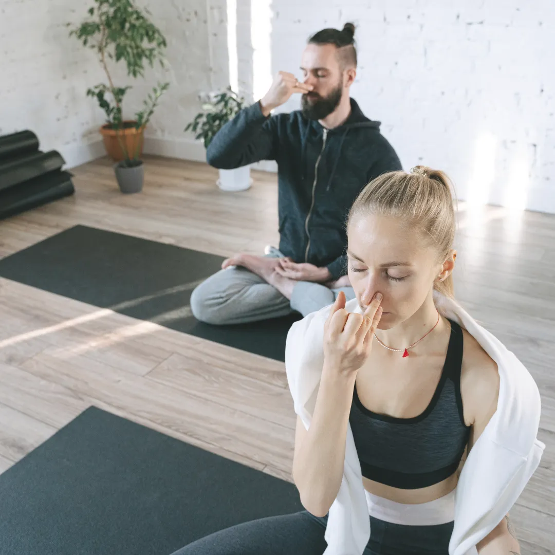 Two athletes in a yoga studio performing alternate nostril breathing, a common breathwork exercise used in HRV-guided recovery protocols to down-shift the autonomic nervous system.