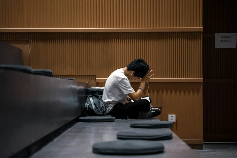 Young person in a white t-shirt sitting alone on auditorium steps with their head in their hands
