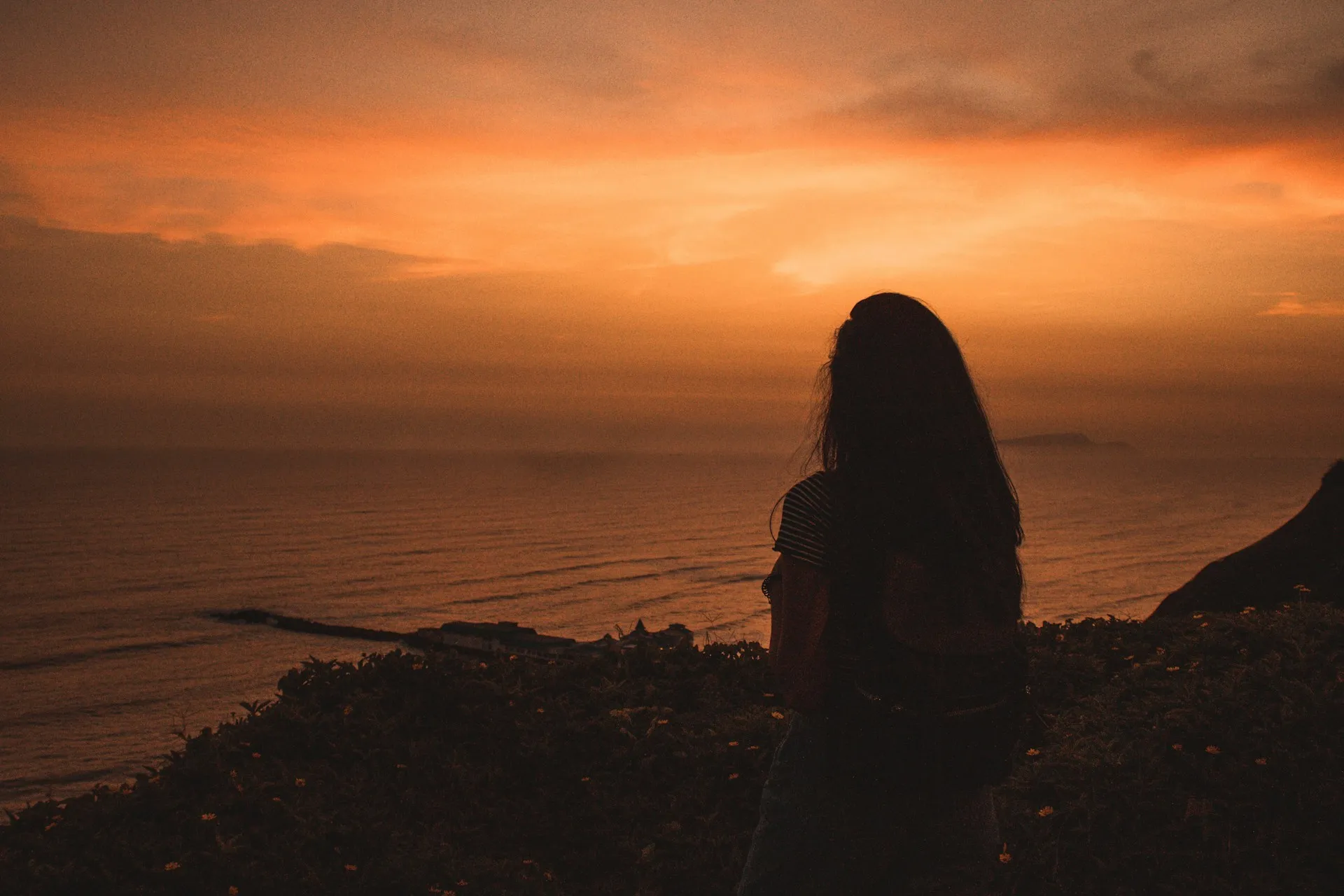 Silhouette of a person looking out over the ocean at an orange sunset