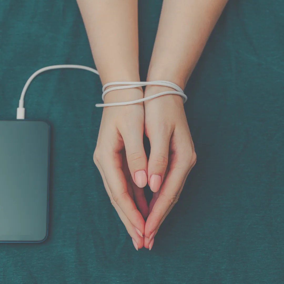 Hands tied with a phone cable symbolizing dependency in the psychology of screen addiction.