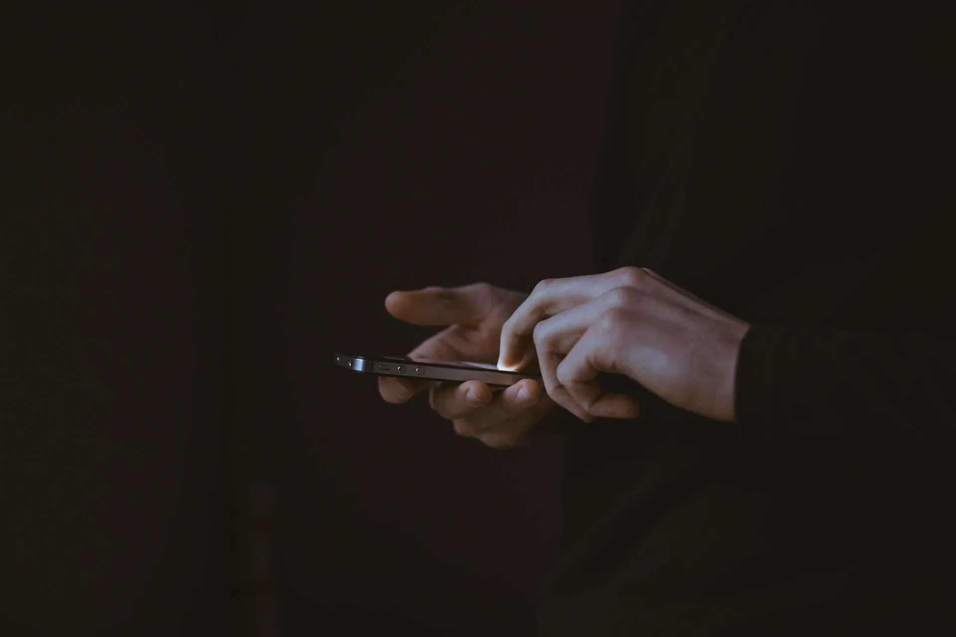 Close-up of hands using a smartphone in a dimly lit room