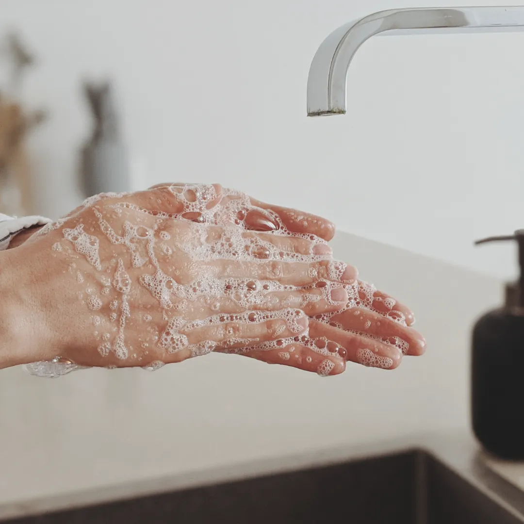 A close-up of a person washing their hands with soap and water at a sink, a key step in preventing the spread of seasonal illnesses like cold and flu.