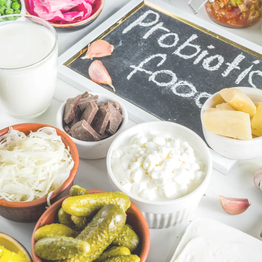 An assortment of probiotic foods including yogurt, kefir, sauerkraut, pickles, and dark chocolate, with a small chalkboard that says "Probiotic Food".